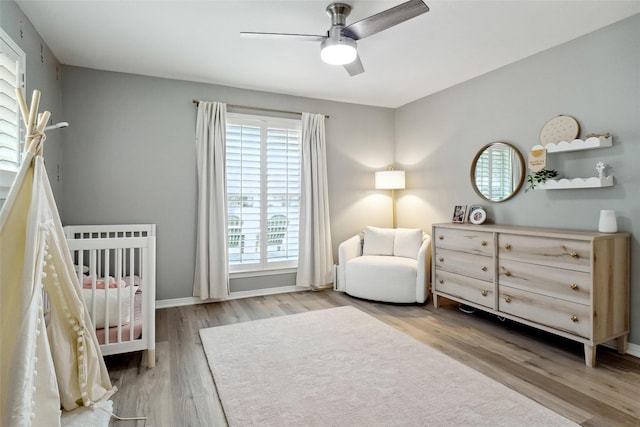 bedroom featuring a nursery area, baseboards, a ceiling fan, and wood finished floors