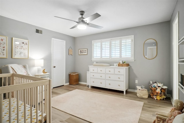 bedroom featuring visible vents, light wood-style flooring, baseboards, and a crib