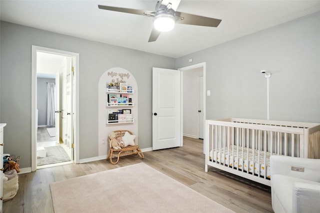 bedroom featuring a crib, ceiling fan, baseboards, and wood finished floors