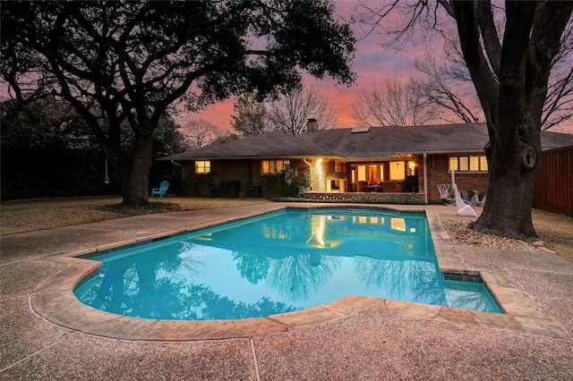 pool at dusk featuring a patio and an outdoor pool