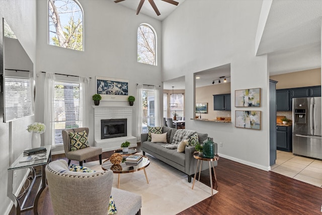 living room with ceiling fan, a fireplace, wood finished floors, and baseboards