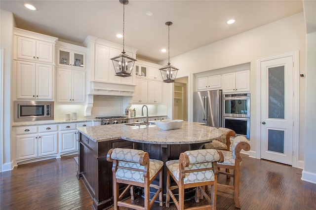 kitchen with a center island with sink, decorative backsplash, custom range hood, stainless steel appliances, and a sink