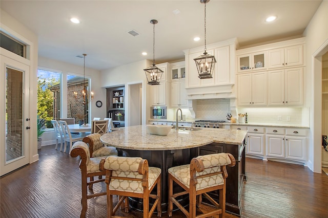 kitchen featuring light stone counters, stainless steel microwave, visible vents, a sink, and a chandelier