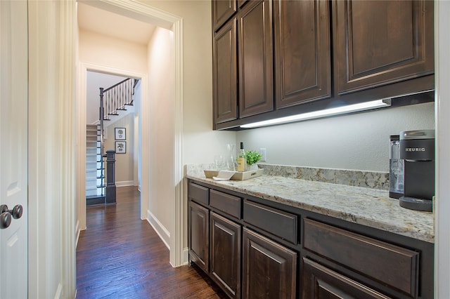 bar featuring dark wood-style floors, a bar, baseboards, and stairs