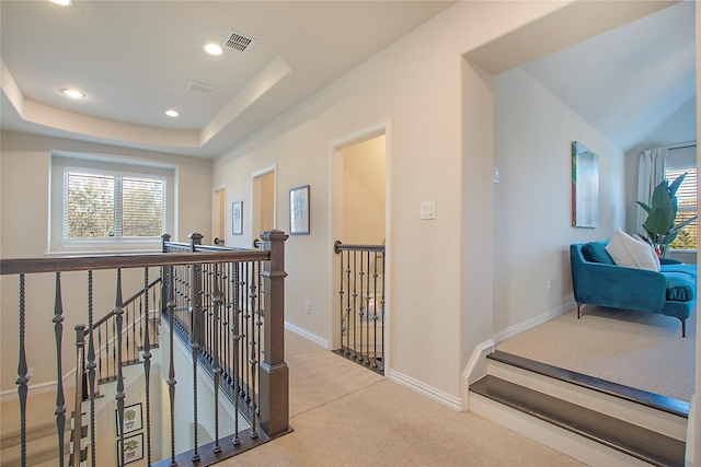 corridor featuring a tray ceiling, recessed lighting, carpet flooring, an upstairs landing, and baseboards