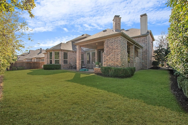 rear view of house featuring a chimney, brick siding, a yard, and a fenced backyard