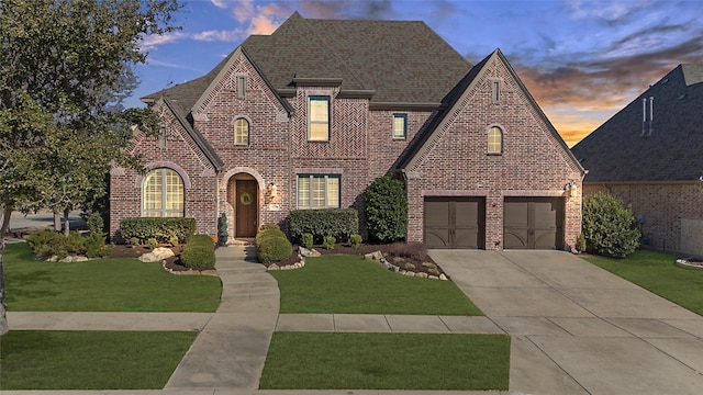 tudor house featuring an attached garage, brick siding, a shingled roof, concrete driveway, and a lawn