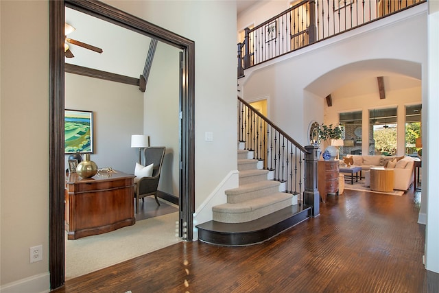 stairway featuring baseboards, arched walkways, a towering ceiling, ceiling fan, and wood finished floors