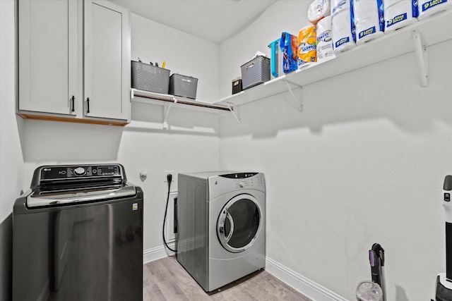 laundry area featuring light wood-style floors, cabinet space, washer and clothes dryer, and baseboards