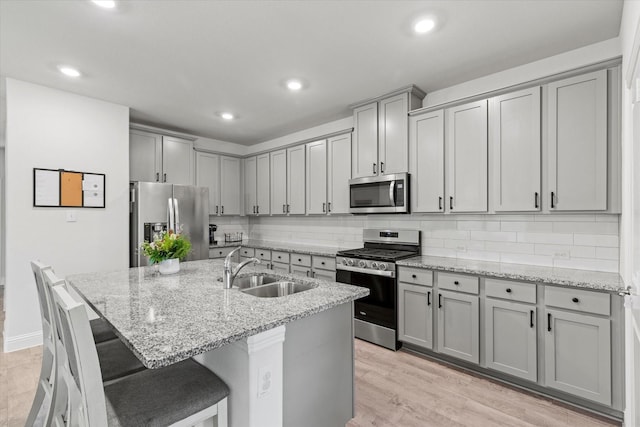 kitchen featuring a sink, appliances with stainless steel finishes, gray cabinets, decorative backsplash, and light stone countertops