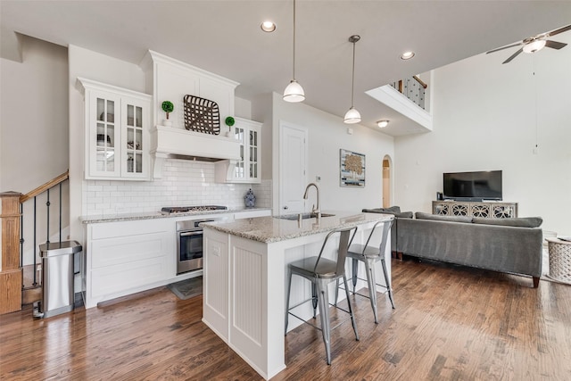 kitchen featuring arched walkways, stainless steel appliances, a sink, open floor plan, and custom exhaust hood