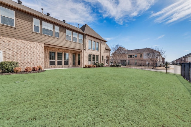 rear view of house with brick siding, a yard, and fence