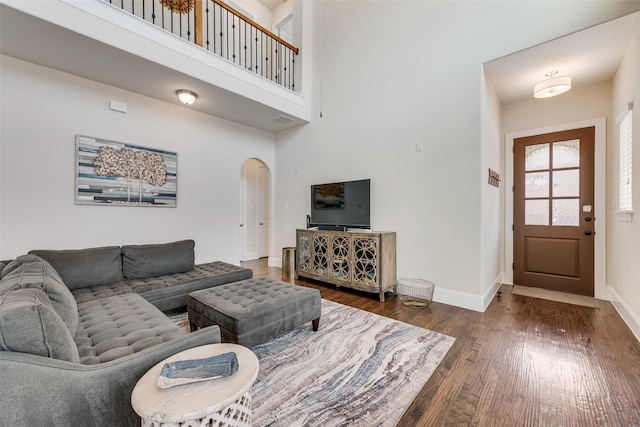 living area with baseboards, visible vents, arched walkways, a towering ceiling, and wood finished floors