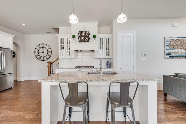 kitchen with tasteful backsplash, arched walkways, dark wood finished floors, freestanding refrigerator, and a sink