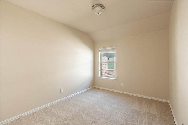 empty room featuring lofted ceiling, light carpet, and baseboards