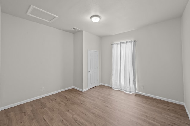 unfurnished room with visible vents, wood finished floors, attic access, and baseboards