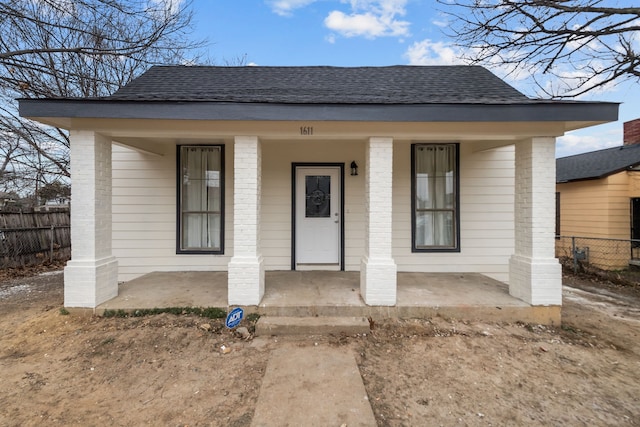 view of front facade featuring a shingled roof, fence, a porch, and brick siding