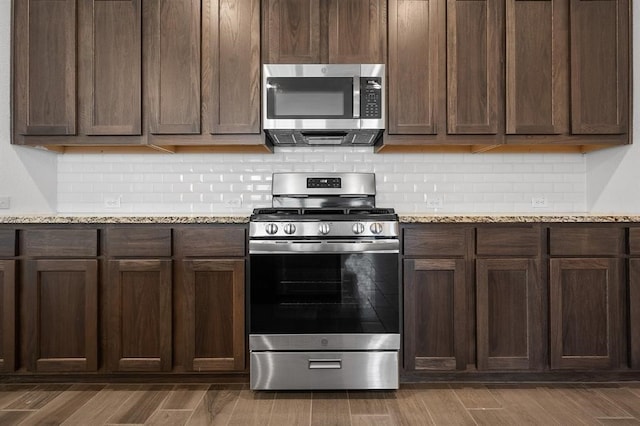 kitchen featuring stainless steel appliances, dark wood-style flooring, backsplash, and light stone countertops