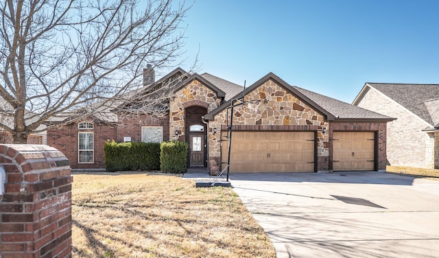 french provincial home with an attached garage, brick siding, driveway, stone siding, and a chimney