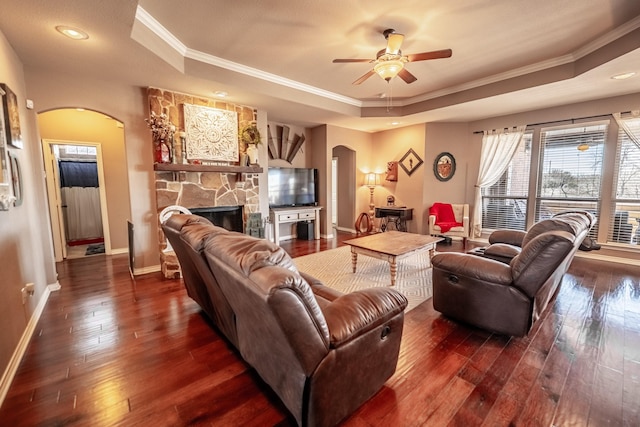 living area featuring a fireplace, arched walkways, a raised ceiling, and dark wood finished floors