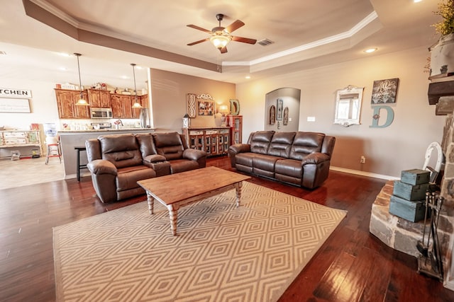 living area featuring dark wood-style floors, arched walkways, a raised ceiling, visible vents, and ornamental molding