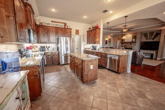 kitchen with a tray ceiling, stainless steel appliances, decorative backsplash, open floor plan, and a peninsula