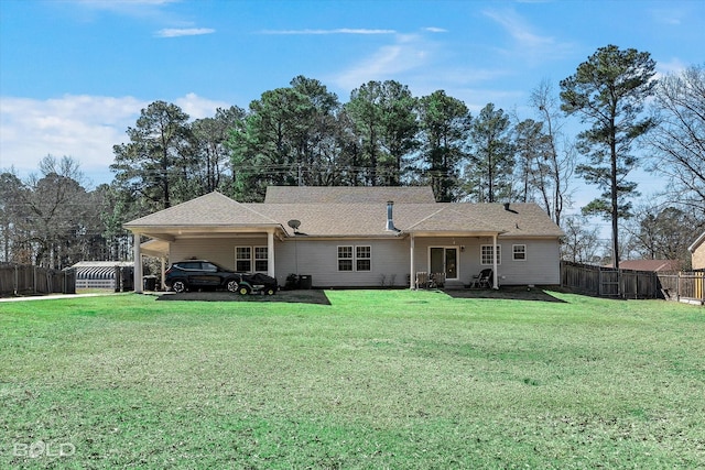 rear view of house with a carport, a lawn, and fence