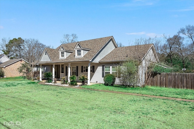 new england style home featuring covered porch, a front lawn, a shingled roof, and fence