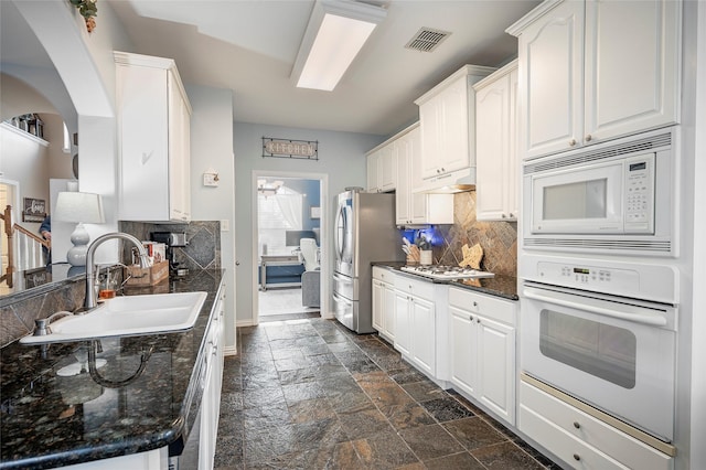 kitchen with white appliances, a sink, backsplash, and stone tile floors