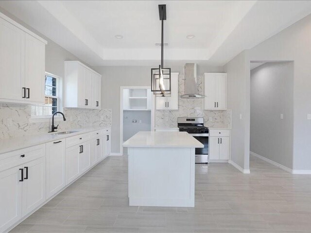 kitchen featuring a sink, a kitchen island, stainless steel gas range, wall chimney exhaust hood, and a raised ceiling