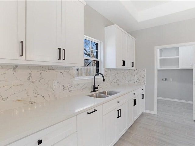 kitchen featuring light countertops, a sink, white cabinetry, and decorative backsplash