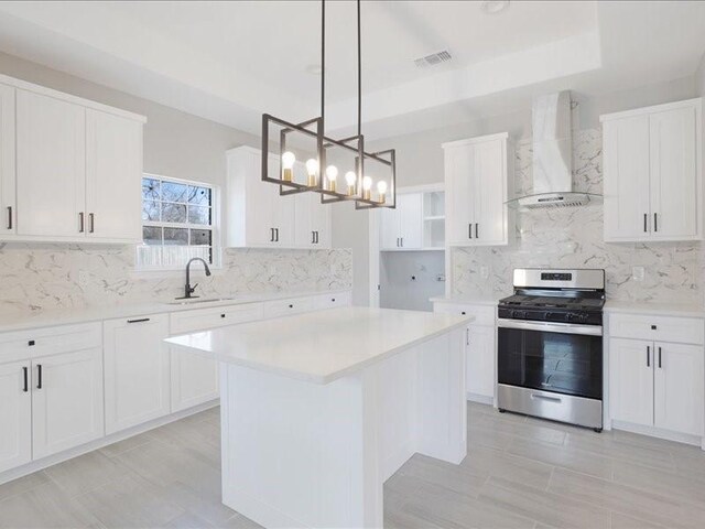 kitchen featuring visible vents, white cabinets, gas range, wall chimney exhaust hood, and a sink
