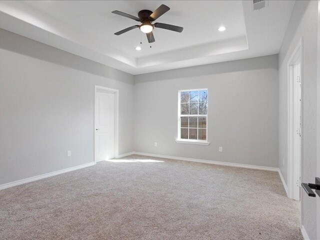 unfurnished room featuring a tray ceiling, carpet, and baseboards