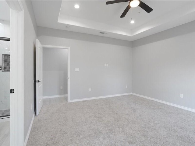 empty room with a tray ceiling, light carpet, baseboards, and recessed lighting