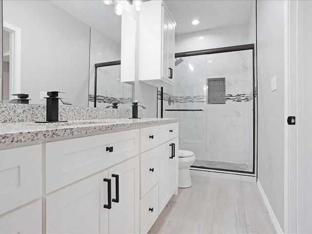 full bathroom with double vanity, a marble finish shower, baseboards, toilet, and a sink