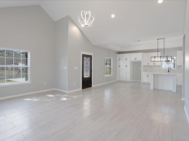unfurnished living room featuring baseboards, high vaulted ceiling, recessed lighting, and an inviting chandelier