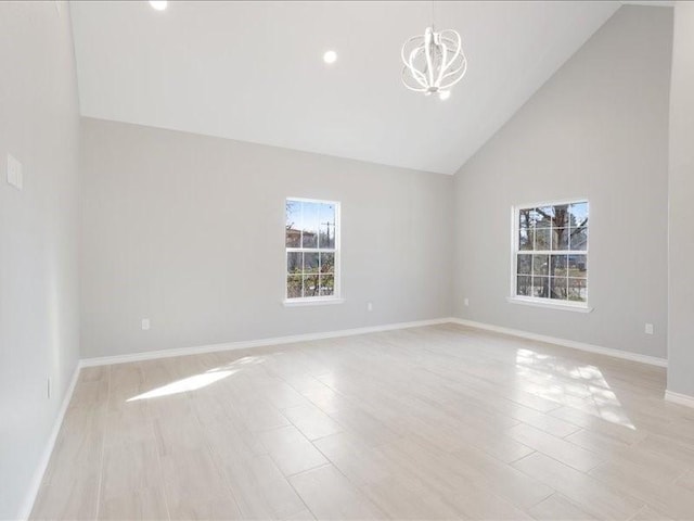 unfurnished room featuring high vaulted ceiling, light wood-style floors, a notable chandelier, and baseboards