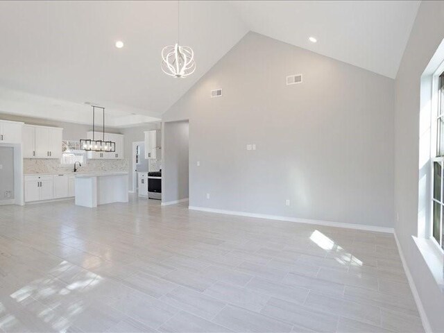 unfurnished living room featuring high vaulted ceiling, visible vents, a notable chandelier, and baseboards
