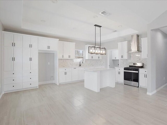 kitchen featuring a tray ceiling, stainless steel range with gas stovetop, a sink, and wall chimney range hood