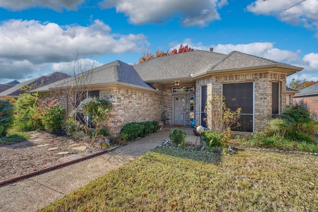 ranch-style house with a shingled roof, a front lawn, and brick siding