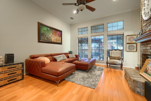 living room featuring a ceiling fan, a brick fireplace, crown molding, and light wood-style flooring