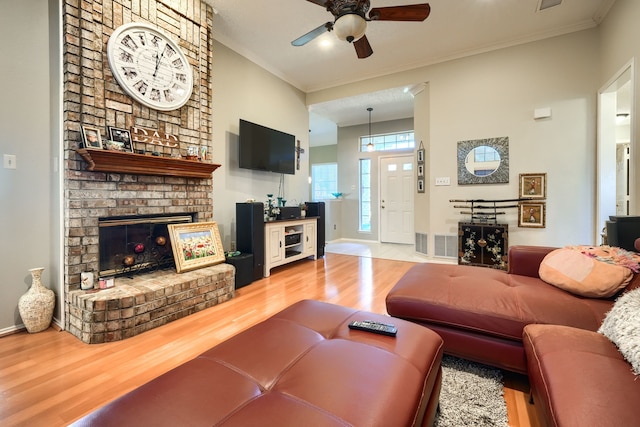 living room with a brick fireplace, crown molding, baseboards, and wood finished floors