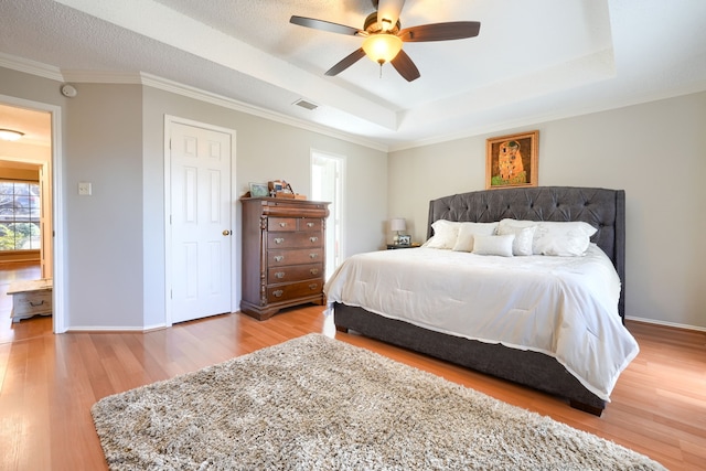 bedroom with baseboards, visible vents, a tray ceiling, and wood finished floors