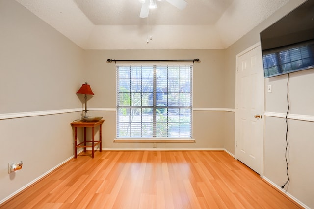 empty room with a ceiling fan, lofted ceiling, baseboards, and wood finished floors