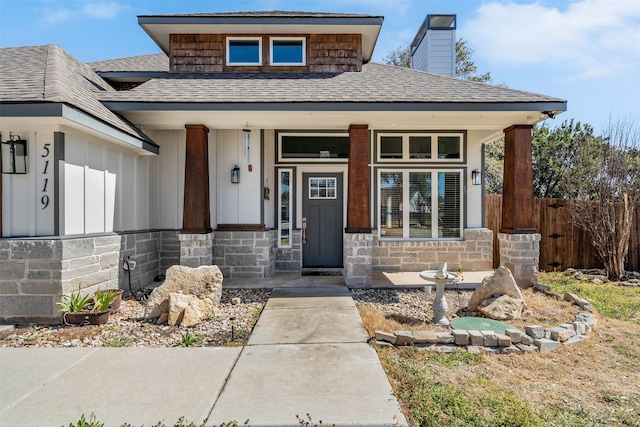 view of front of property featuring stone siding, fence, a porch, and roof with shingles