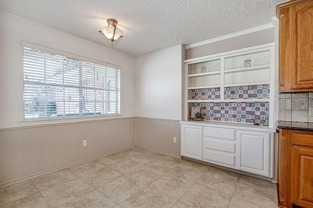 interior space with light tile patterned floors, a textured ceiling, and wainscoting