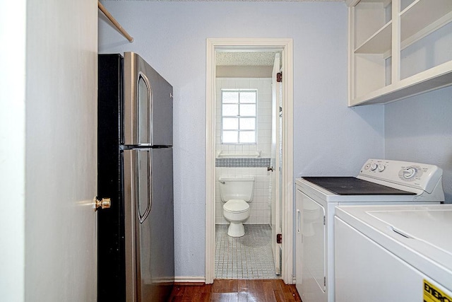 laundry room with laundry area, washing machine and dryer, dark wood-style flooring, and tile walls