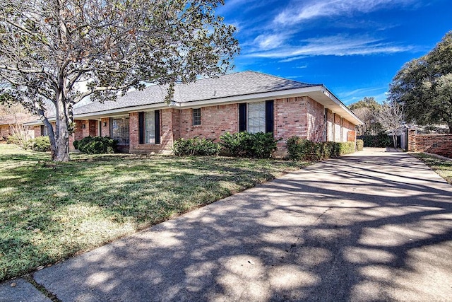 view of front of property featuring driveway, roof with shingles, a front lawn, and brick siding