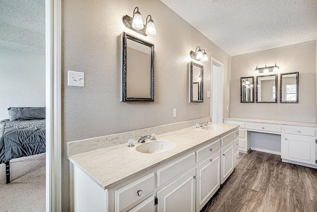 bathroom with a textured ceiling, double vanity, wood finished floors, and a sink