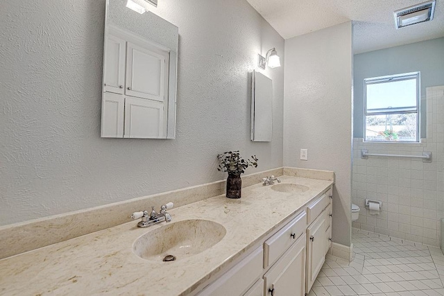 full bathroom with toilet, double vanity, visible vents, and a sink